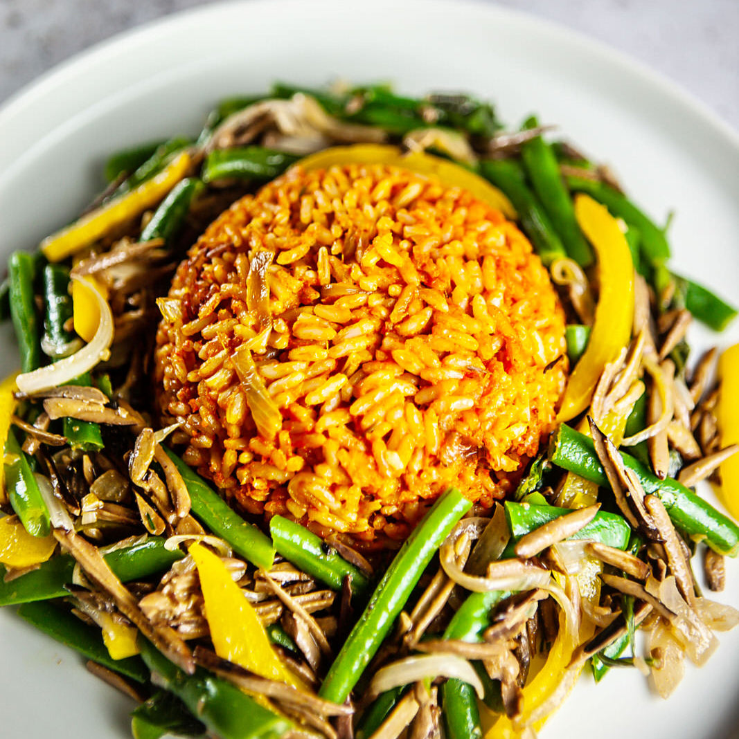 Plate of Nigerian jollof rice with a vegetable and mushroom stirfry