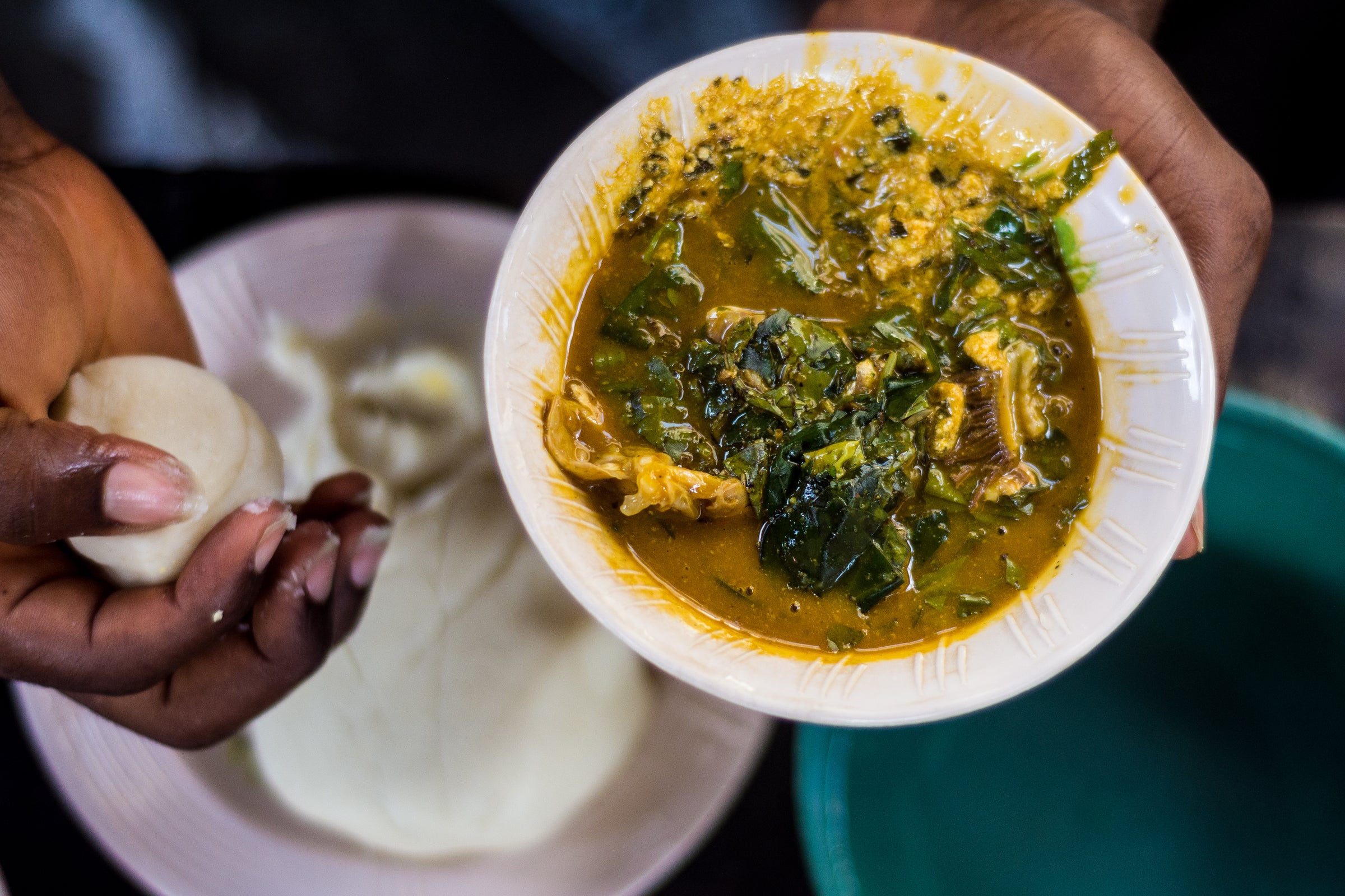 Hand dipping pounded yam into a bowl of vibrant Nigerian soup.